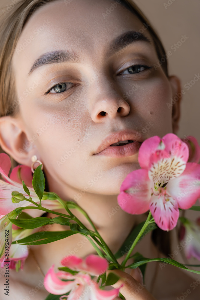 close up portrait of sensual woman with natural makeup near pink flowers isolated on beige. close up portrait of sensual woman with natural makeup near pink flowers isolated on beige.