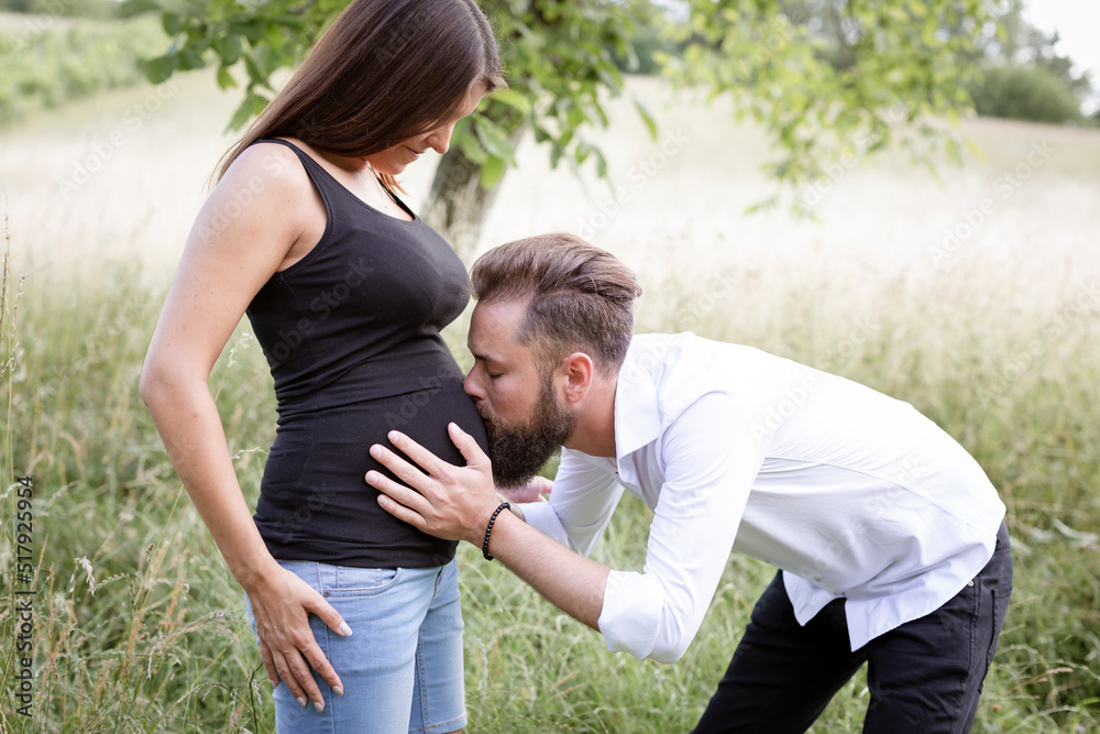 Obraz premium pretty young pregnant woman with black shirt is standing with her boyfriend in a high meadow and they are happy and full of anticipation for the baby