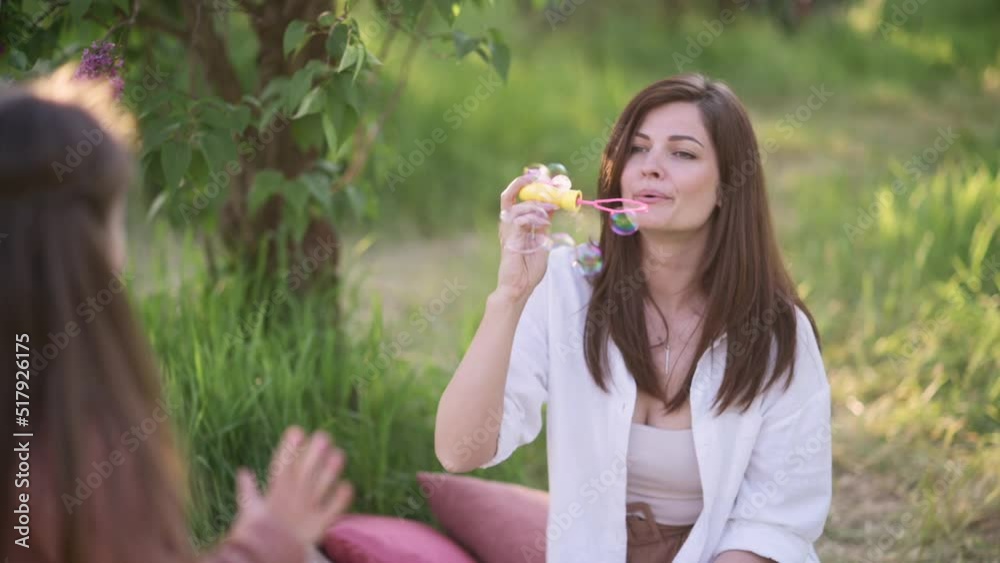 Mom and daughter are having fun. Young woman blowing soap bubbles in the park. Slow motion. Mom and daughter are having fun. Young woman blowing soap bubbles in the park. Slow motion.