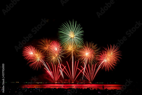 Colorful magical fireworks showing on sea in celebration festival with city lighting and black sky background. 
