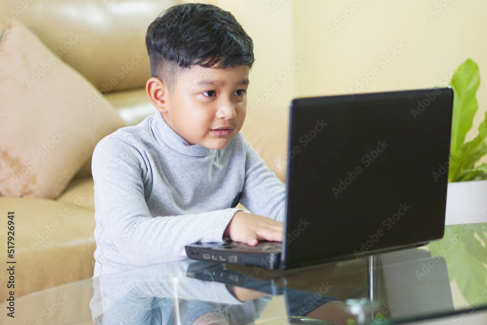 The Asian boy focusing working on laptop and have a cute smile The Asian boy focusing working on laptop and have a cute smile