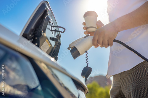 close-up of a man charging an electric car with coffee in his hands. Eco friendly alternative energy concept