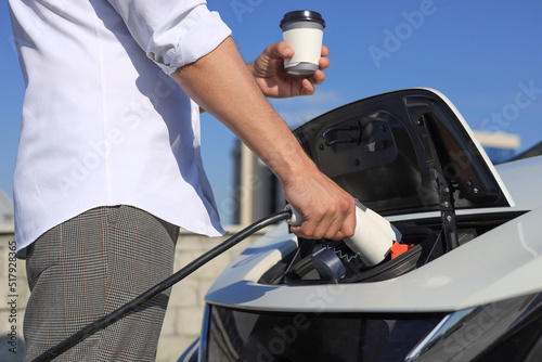 close-up of a man charging an electric car with coffee in his hands. Eco friendly alternative energy concept