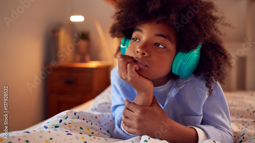 Boy Thinking In Bedroom Lying On Bed Wearing Headphones