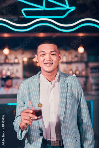 A handsome asian man looking dapper enjoying Cuba libre or Rum and Cola drink at a trendy outdoor bar or cafe.