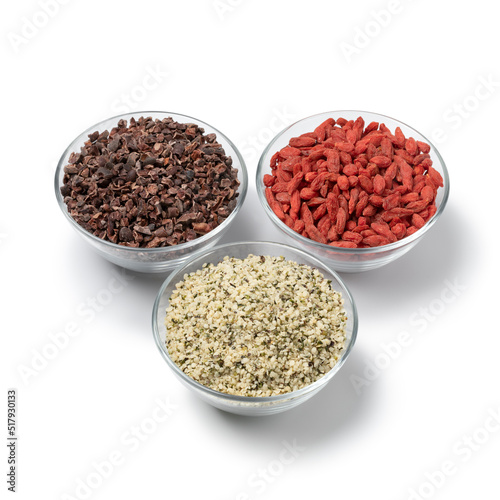 Three glass bowls with superfood, dried goji berries , cacao nibs and hemp seed isolated on white background