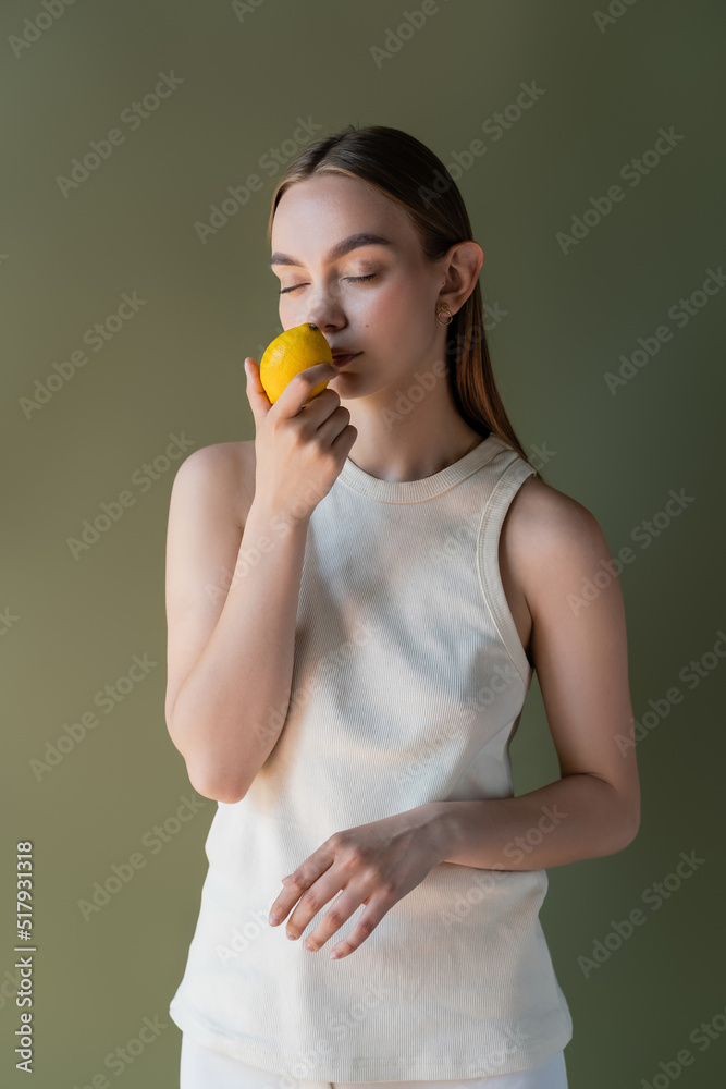 woman in white tank top smelling aromatic lemon with closed eyes isolated on green. woman in white tank top smelling aromatic lemon with closed eyes isolated on green.