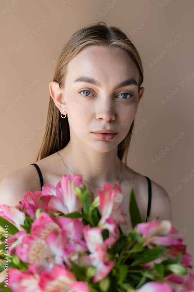 young woman with perfect skin looking at camera near alstroemeria flowers isolated on beige. young woman with perfect skin looking at camera near alstroemeria flowers isolated on beige.