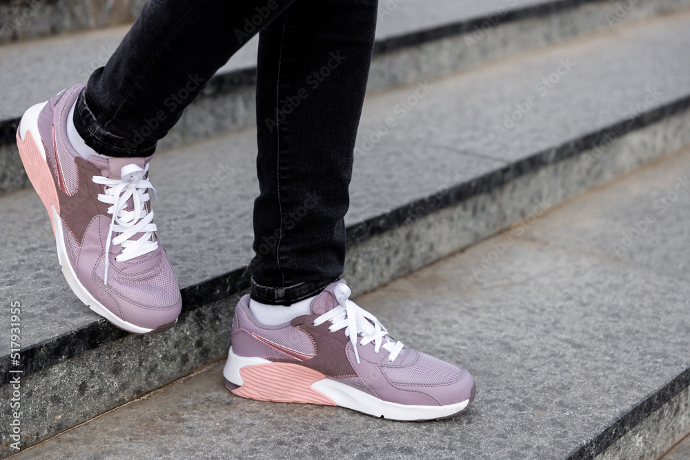 cropped image of female legs in shoes. Woman in pink sneakers descend stairs