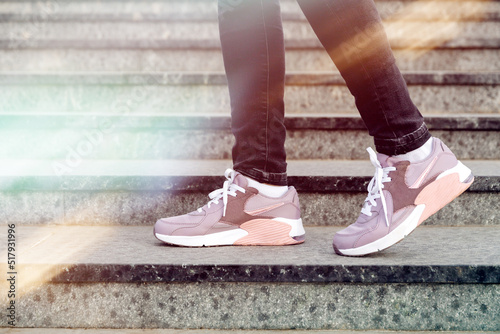 cropped image of female legs in shoes. Woman in pink sneakers descend stairs