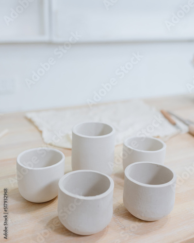 woman ceramist in the workshop makes mugs out of clay. a small business or hobby is the creation of ceramic products. an oriental young woman ceramist makes dishes and vases out of clay. handmade