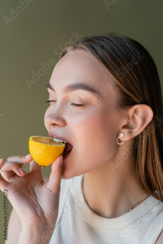 young woman with closed eyes biting juicy lemon isolated on green.