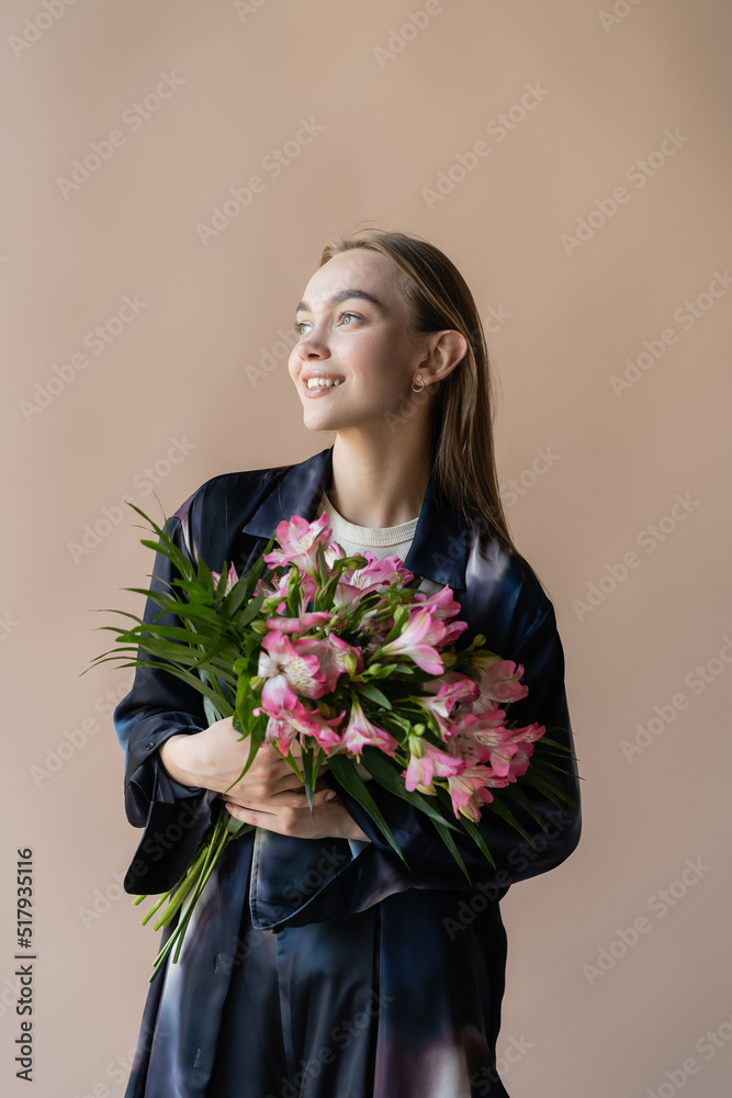 happy and trendy woman with fresh floral bouquet looking away isolated on beige. happy and trendy woman with fresh floral bouquet looking away isolated on beige.