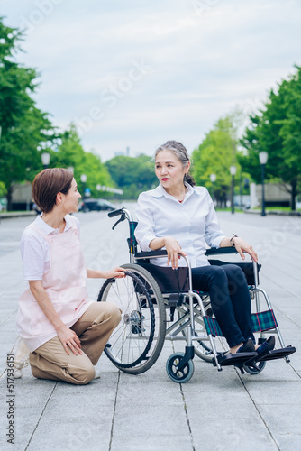 車椅子の女性と介護するエプロン姿の女性 © maru54