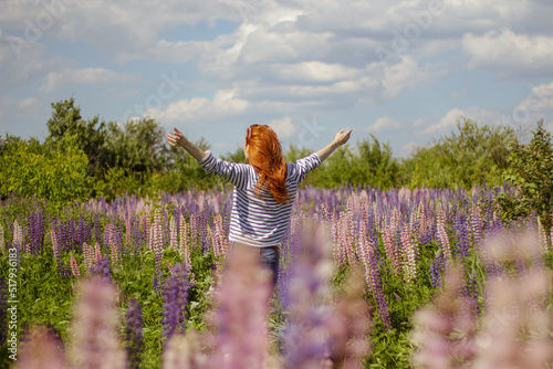 redhead young woman dancing in the field of lupines