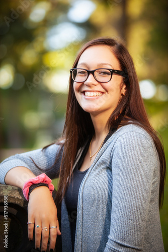 portrait of a pretty teenaged girl with dark hair and glasses seated in a park