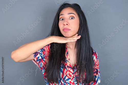 Young latin woman wearing colorful dress over grey backgrogund cutting throat with hand as knife, threaten aggression with furious violence.