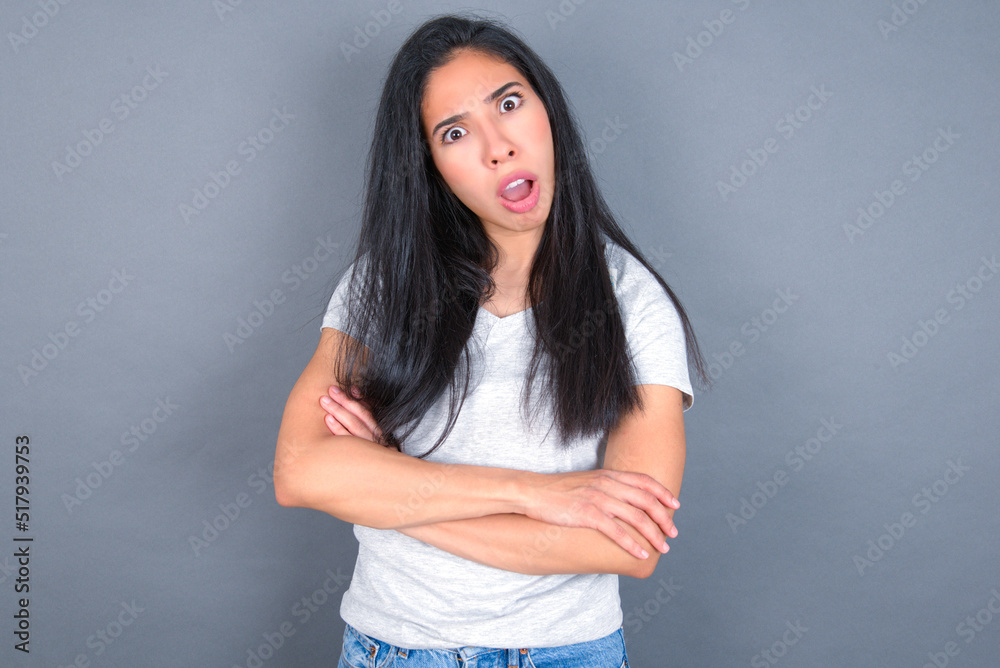 Shocked embarrassed young beautiful brunette woman wearing white t-shirt over grey background keeps mouth widely opened. Hears unbelievable novelty stares in stupor Shocked embarrassed young beautiful brunette woman wearing white t-shirt over grey background keeps mouth widely opened. Hears unbelievable novelty stares in stupor
