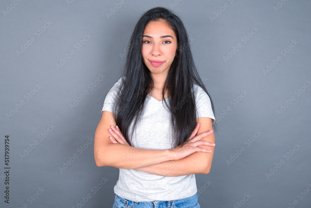 Self confident serious calm young beautiful brunette woman wearing white t-shirt over grey background stands with arms folded. Shows professional vibe stands in assertive pose. Self confident serious calm young beautiful brunette woman wearing white t-shirt over grey background stands with arms folded. Shows professional vibe stands in assertive pose.