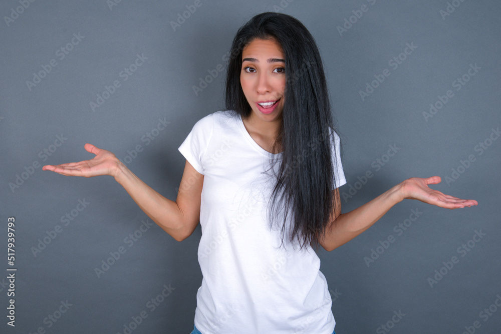 So what? Portrait of arrogant young beautiful brunette woman wearing white t-shirt over grey background shrugging hands sideways smiling gasping indifferent, telling something obvious. So what? Portrait of arrogant young beautiful brunette woman wearing white t-shirt over grey background shrugging hands sideways smiling gasping indifferent, telling something obvious.