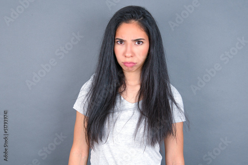 Offended dissatisfied young beautiful brunette woman wearing white t-shirt over grey background with moody displeased expression at camera being disappointed by something