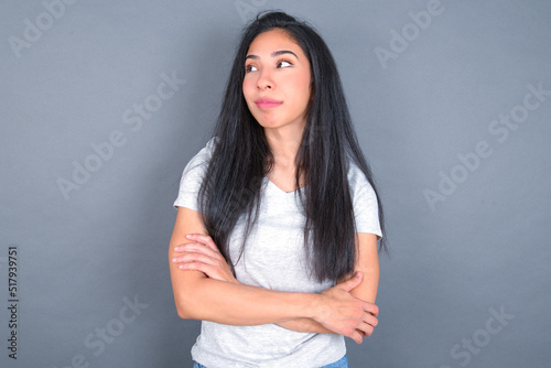 Pleased young beautiful brunette woman wearing white t-shirt over grey background keeps hands crossed over chest looks happily aside