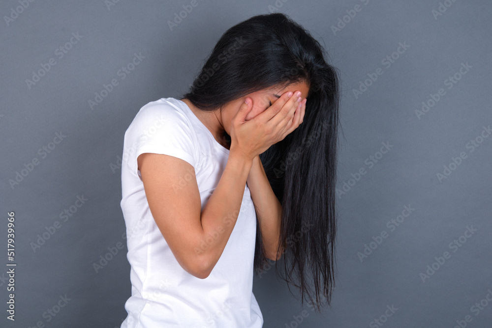 Sad young beautiful brunette woman wearing white t-shirt over grey background covering face with hands and crying. Sad young beautiful brunette woman wearing white t-shirt over grey background covering face with hands and crying.