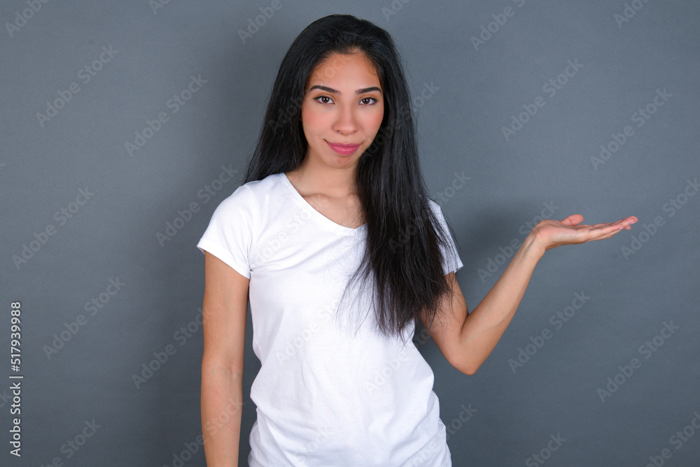 Positive glad young beautiful brunette woman wearing white t-shirt over grey says: wow how exciting it is, has amazed expression, shows something on blank space with open hand. Advertisement concept. Positive glad young beautiful brunette woman wearing white t-shirt over grey says: wow how exciting it is, has amazed expression, shows something on blank space with open hand. Advertisement concept.