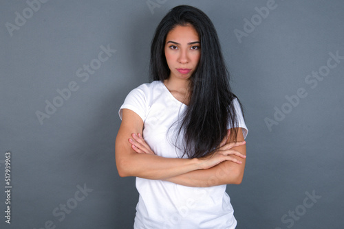 Picture of angry young beautiful brunette woman wearing white t-shirt over grey background looking camera.
