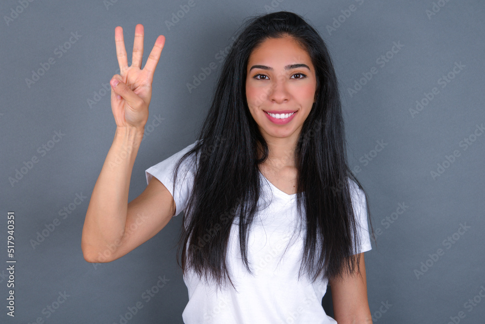 young beautiful brunette woman wearing white t-shirt over grey background showing and pointing up with fingers number three while smiling confident and happy. young beautiful brunette woman wearing white t-shirt over grey background showing and pointing up with fingers number three while smiling confident and happy.