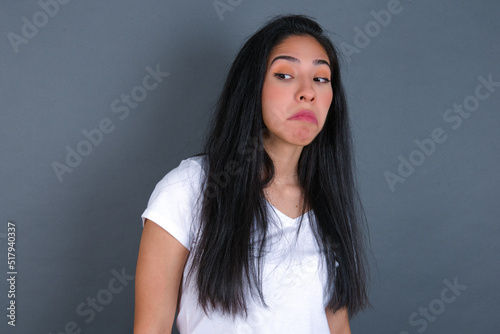 young beautiful brunette woman wearing white t-shirt over grey background with snobbish expression curving lips and raising eyebrows, looking with doubtful and skeptical expression, suspect and doubt.