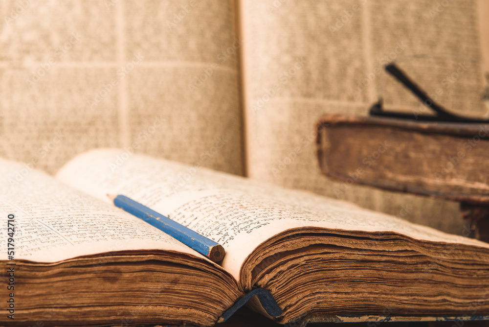 Old worn shabby jewish books in leather binding and open blurred Torah in the background. Closeup. Selective focus.