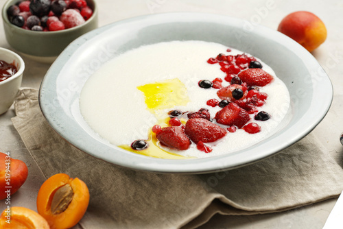 Traditional breakfast semolina porridge - creamy pudding with butter, frozen berries and fresh apricots in a grey plate