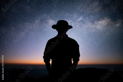 Silhouette of young traveler and backpacker standing alone on top of the mountain and watched the beautiful view of night sky, star and milky way over the sky.