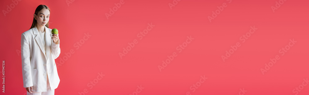 pretty woman in white trendy blazer holding ripe apple isolated on pink, banner. pretty woman in white trendy blazer holding ripe apple isolated on pink, banner.