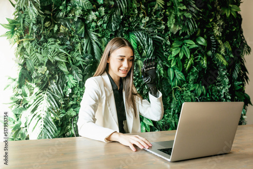 A young woman with a prosthetic bionic arm communicates video call on laptop. Online work, distance learning