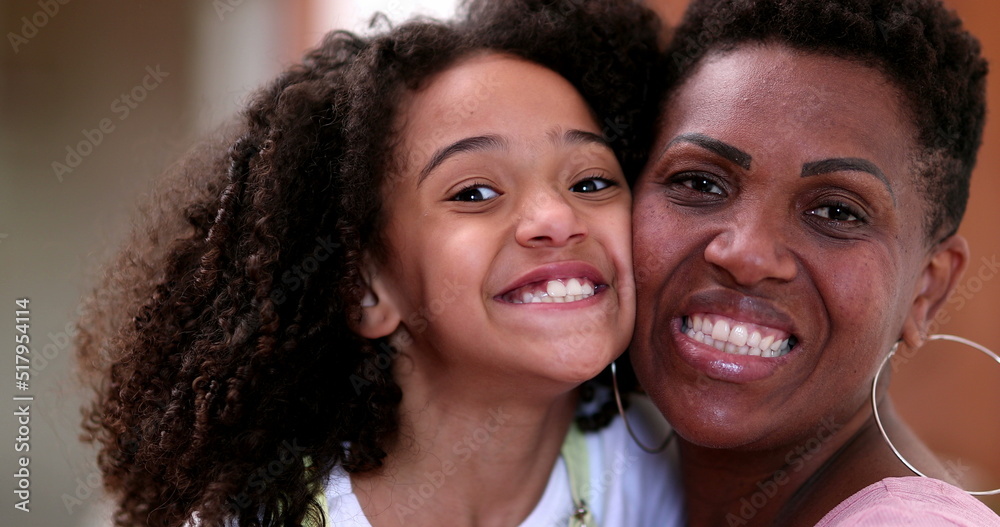 Happy African mother and daughter posing to camera smiling, cheek to cheek Happy African mother and daughter posing to camera smiling, cheek to cheek