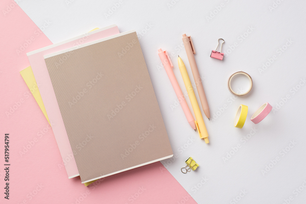 Back to school concept. Top view photo of stationery stack of copybooks pens binder clips and adhesive tape on bicolor pink and white background Back to school concept. Top view photo of stationery stack of copybooks pens binder clips and adhesive tape on bicolor pink and white background