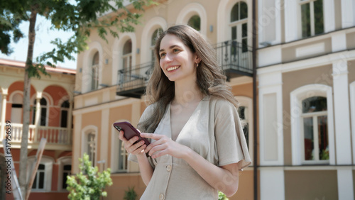 Young woman using smartphone outdoors. Joyful smiling woman girl looking at mobile phone in a city. Communication, technology, connection, lifestyle, summer vacation and travel concept