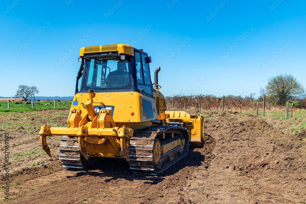 Working bulldozer clears the area before construction. Rear view. Blue sky background.