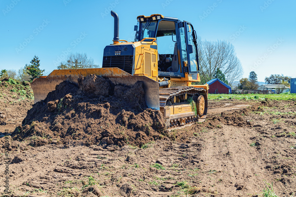 Working bulldozer clears the area before construction. Blue sky background. - obrazy, fototapety, plakaty 