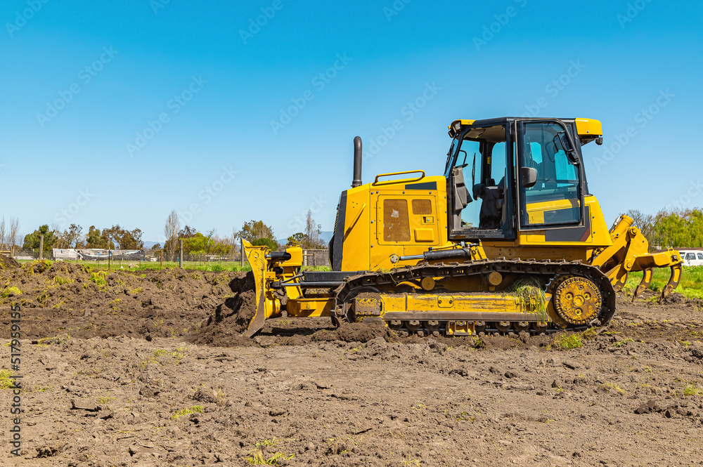 Side view working bulldozer clears the area before construction. Blue sky background. Side view working bulldozer clears the area before construction. Blue sky background.