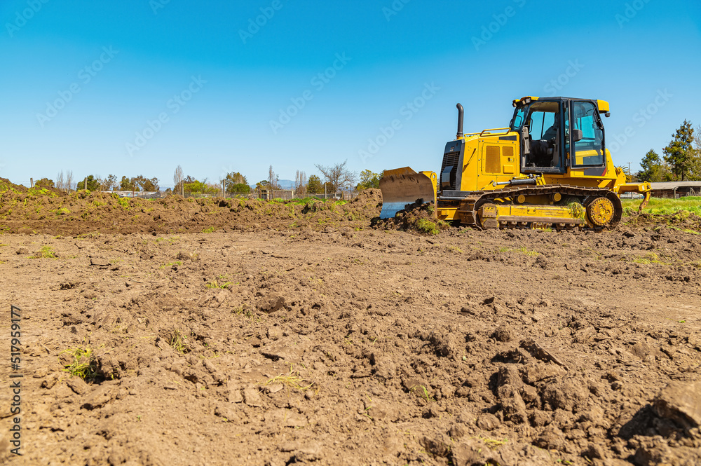 Sidet view of a yellow bulldozer on a plot of land. A bulldozer clears the area. Blue sky background. Sidet view of a yellow bulldozer on a plot of land. A bulldozer clears the area. Blue sky background.