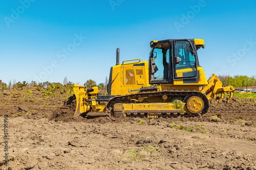 Side view working bulldozer clears the area before construction. Blue sky background.