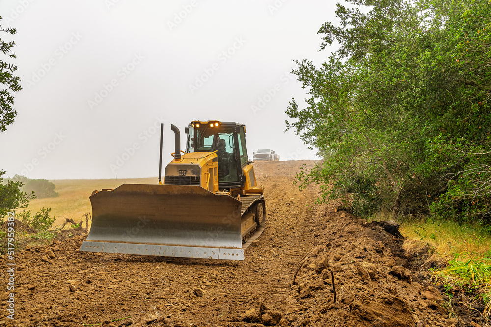 Working bulldozer clears the area before construction. Blue sky background.