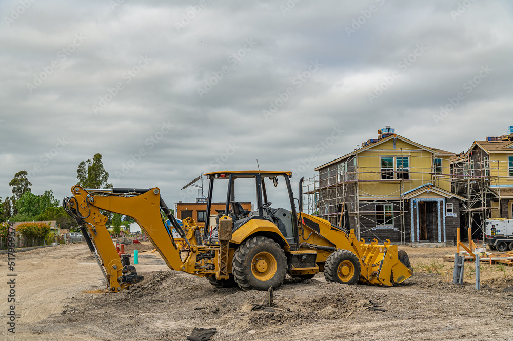 Excavator at the construction site. Frame houses with sip panels in the background. Cloudy sky.
