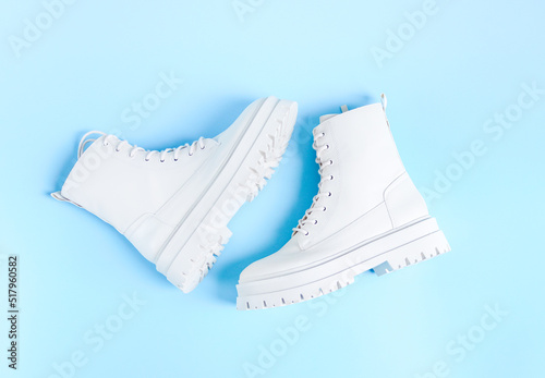 White demi-season martens boots made of eco-leather with a rough sole lie in the center on a blue.. photo