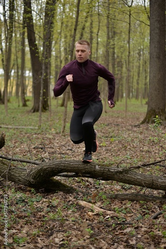 A man in sportswear is jogging. Path in the forest. Active lifestyle. Cross country running. A man jumps over a branch.