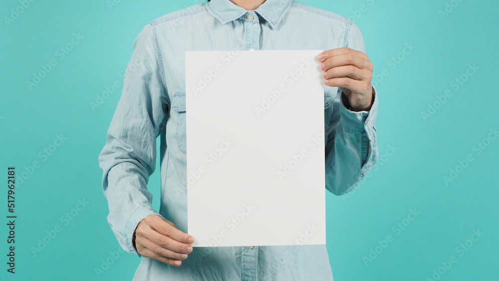 The body part of a woman and two hands holding a white sheet a4 board on a green mint background.Vertical line The body part of a woman and two hands holding a white sheet a4 board on a green mint background.Vertical line