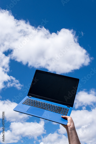 Hand holding a blue laptop and blue sky as background 	